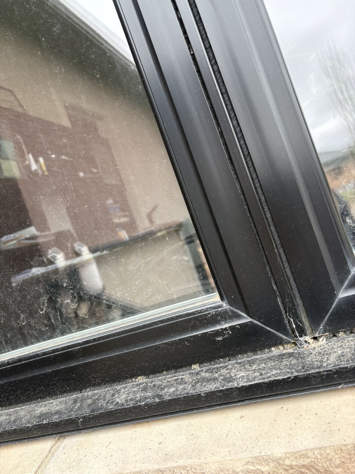 Black window frames and the lower sill before cleaning, with dust and buildup