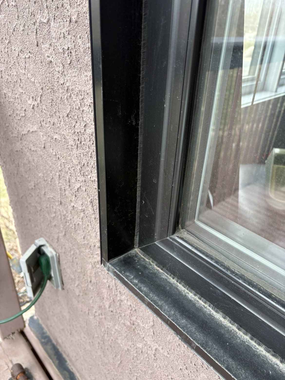 The lower corner of an exterior window frame and sill before cleaning, with dust and buildup